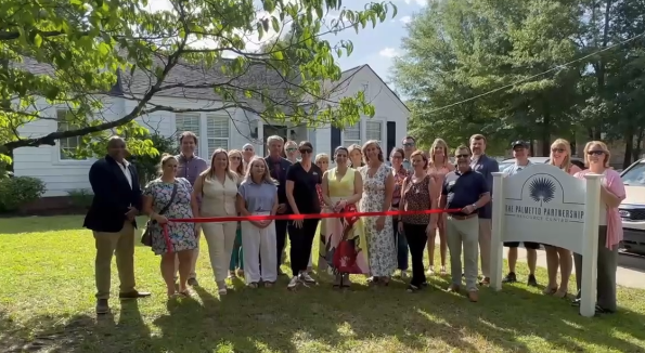 A group of individuals cutting a red ribbon in honor of the opening of The Palmetto Partnership's new location